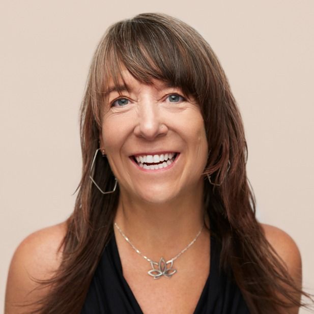Smiling woman with long brown hair wearing a black top and butterfly necklace on a neutral background