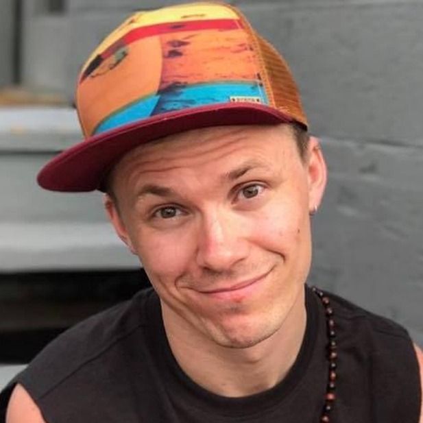 Person wearing a colorful cap and black shirt, smiling with a slight head tilt.