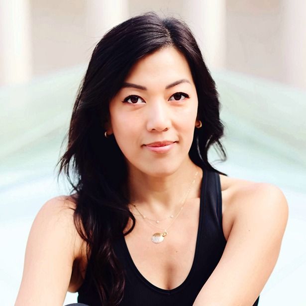 Woman with long dark hair wearing a black top, sitting outdoors with a soft, blurred background