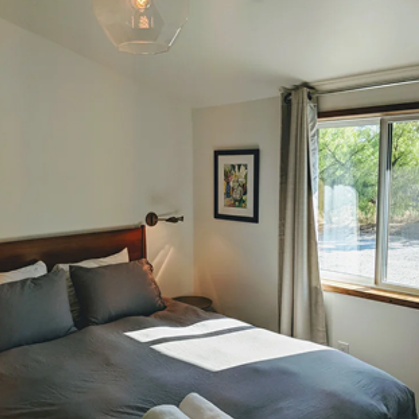 Bedroom with dark gray bedding, a wooden headboard, and a window with curtains letting in sunlight.
