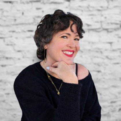 Person doing a yoga boat pose on a mat in a bright studio, smiling toward the camera.