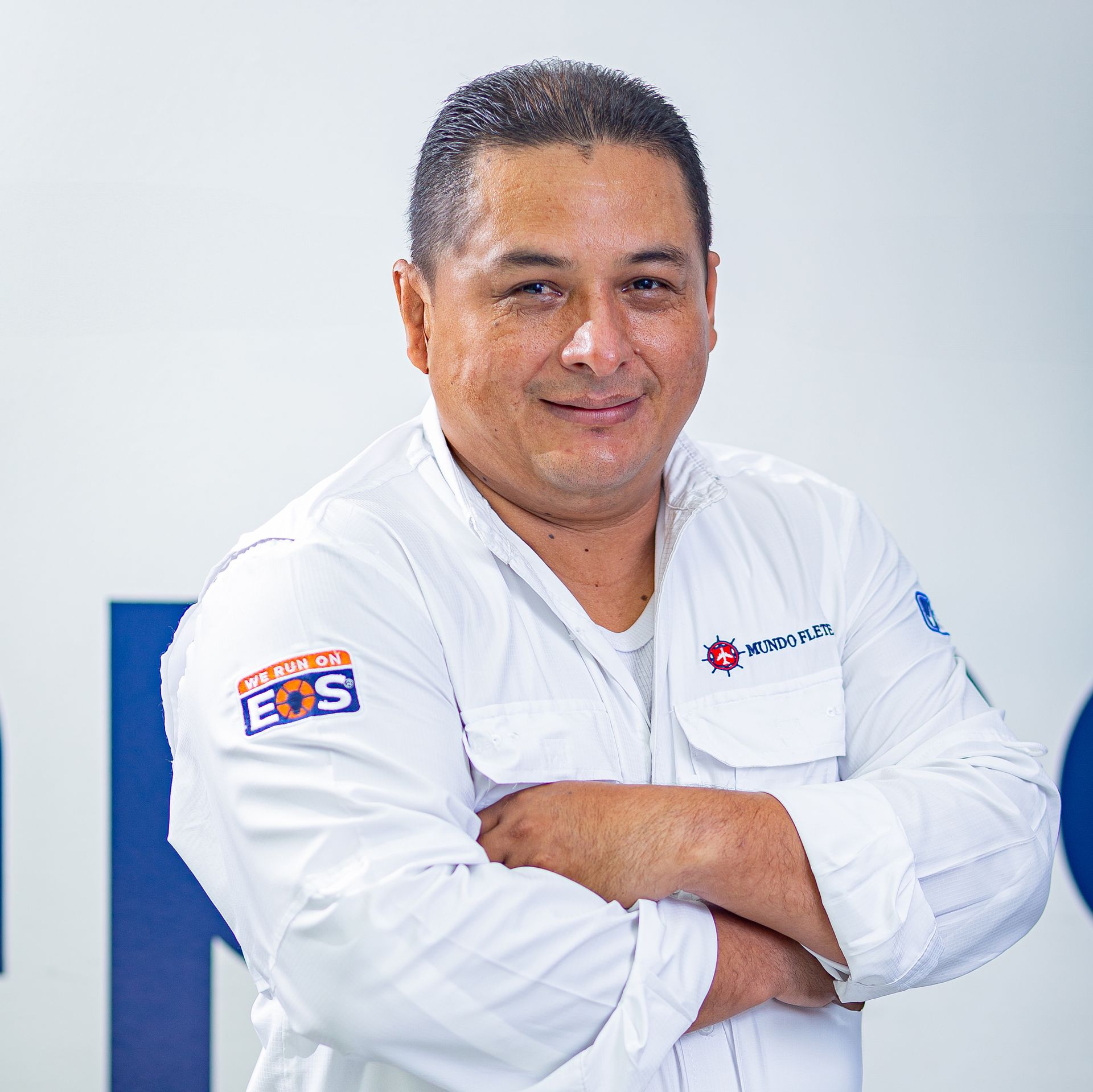 Retrato de una persona con uniforme blanco, con los brazos cruzados, de pie sobre un fondo claro.