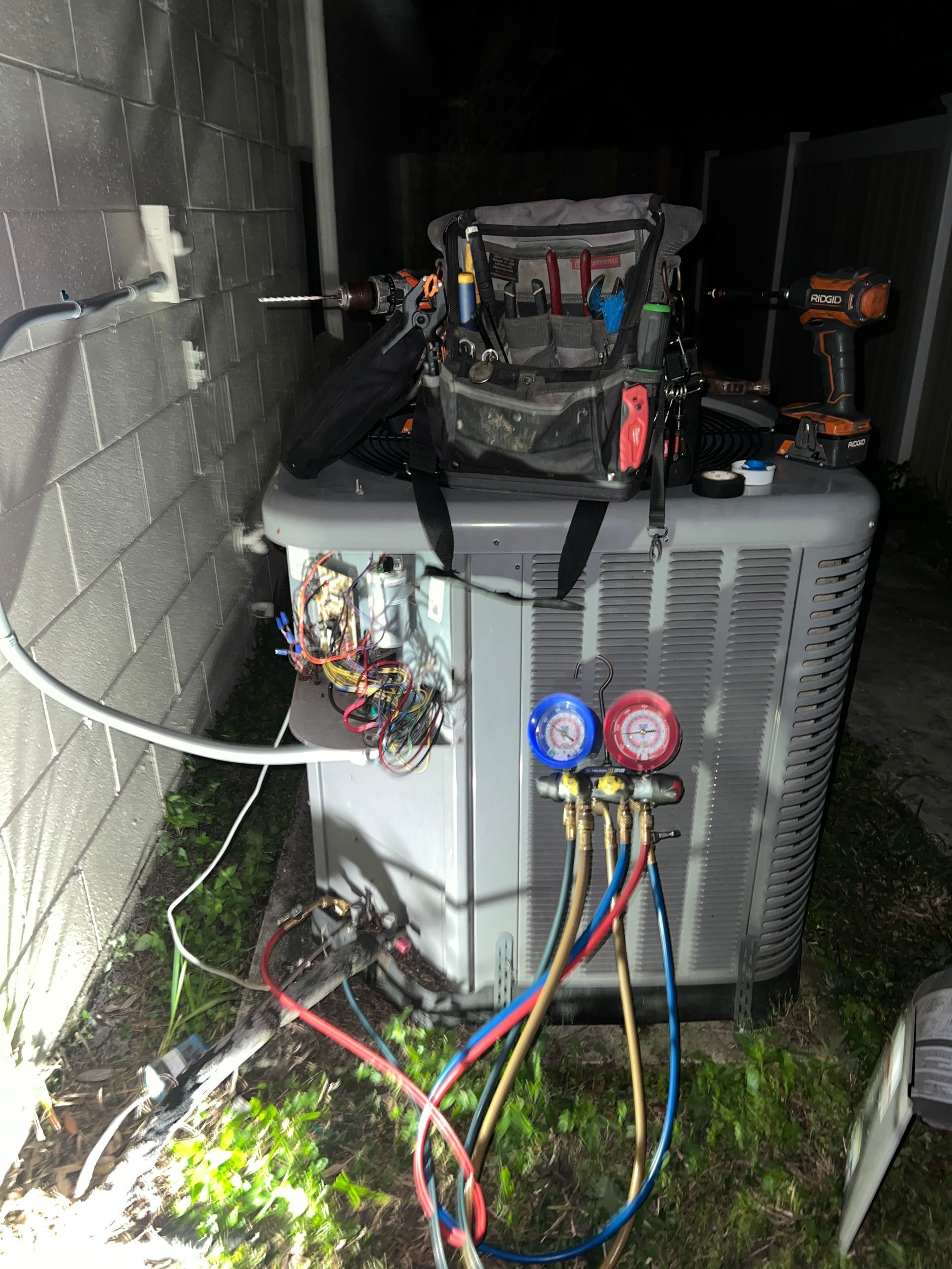 an air conditioner is being serviced outside of a house at night .