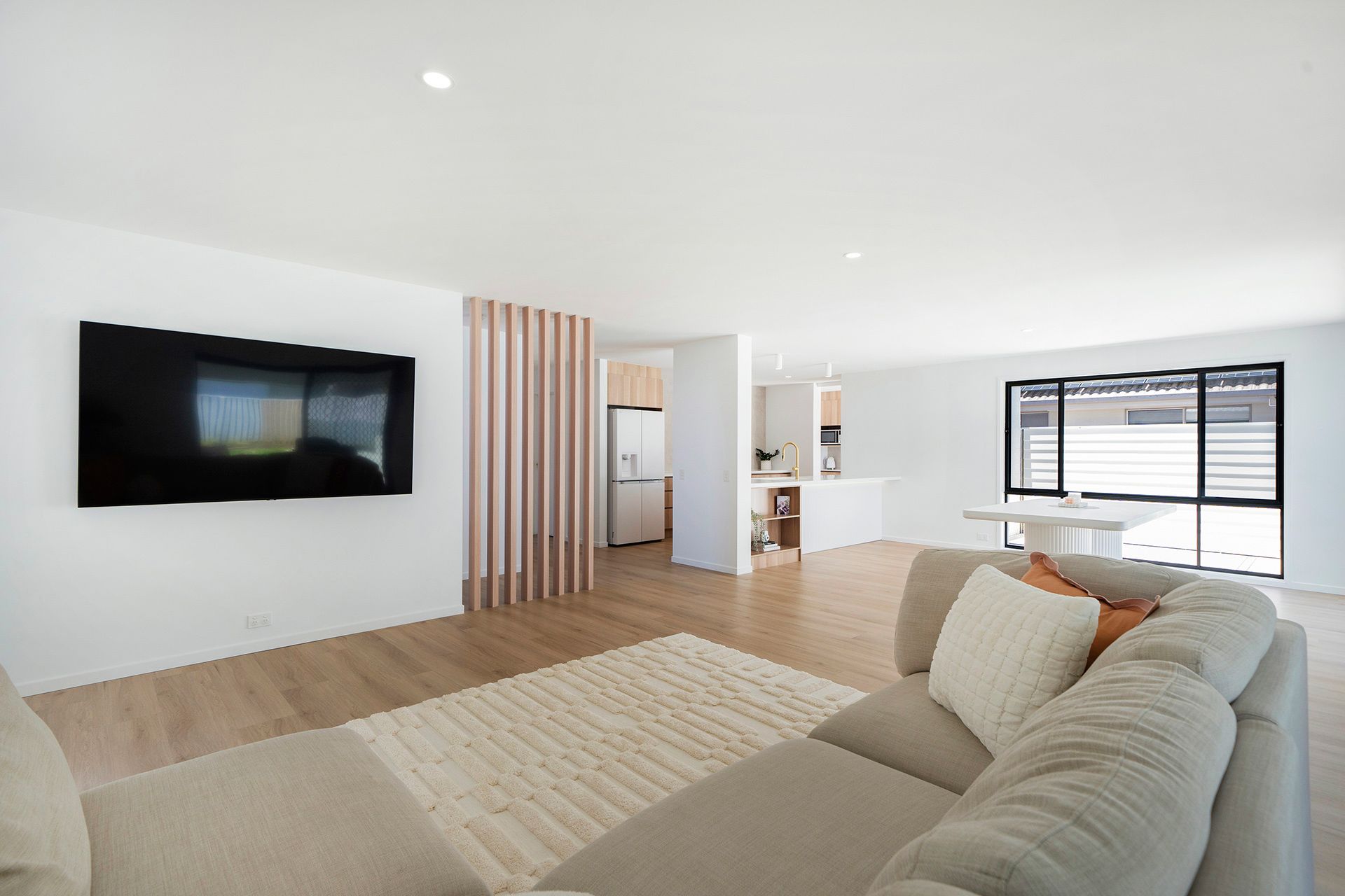 Bright modern living room with wall-mounted TV, beige sectional sofa, light wood floors— Reynolds Built In Caloundra, QLD
