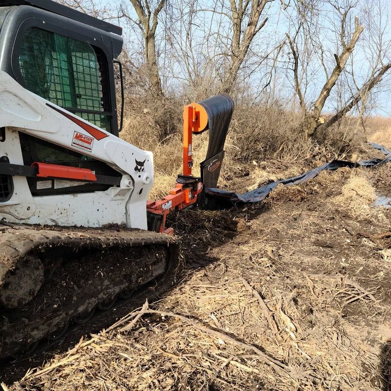 White skid steer clearing brush on a wooded hillside with an orange attachment