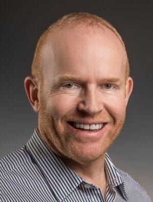 A bald man with red hair is smiling for the camera while wearing a striped shirt.