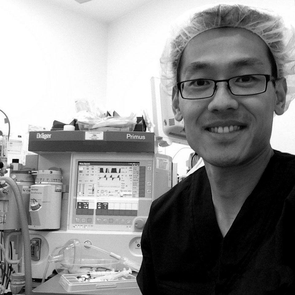 A man wearing glasses and a surgical cap is smiling in an operating room.