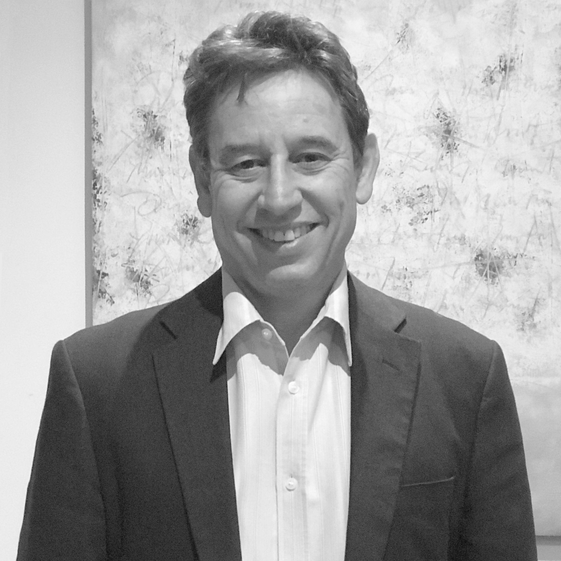 A man in a suit and white shirt is smiling in front of a painting.