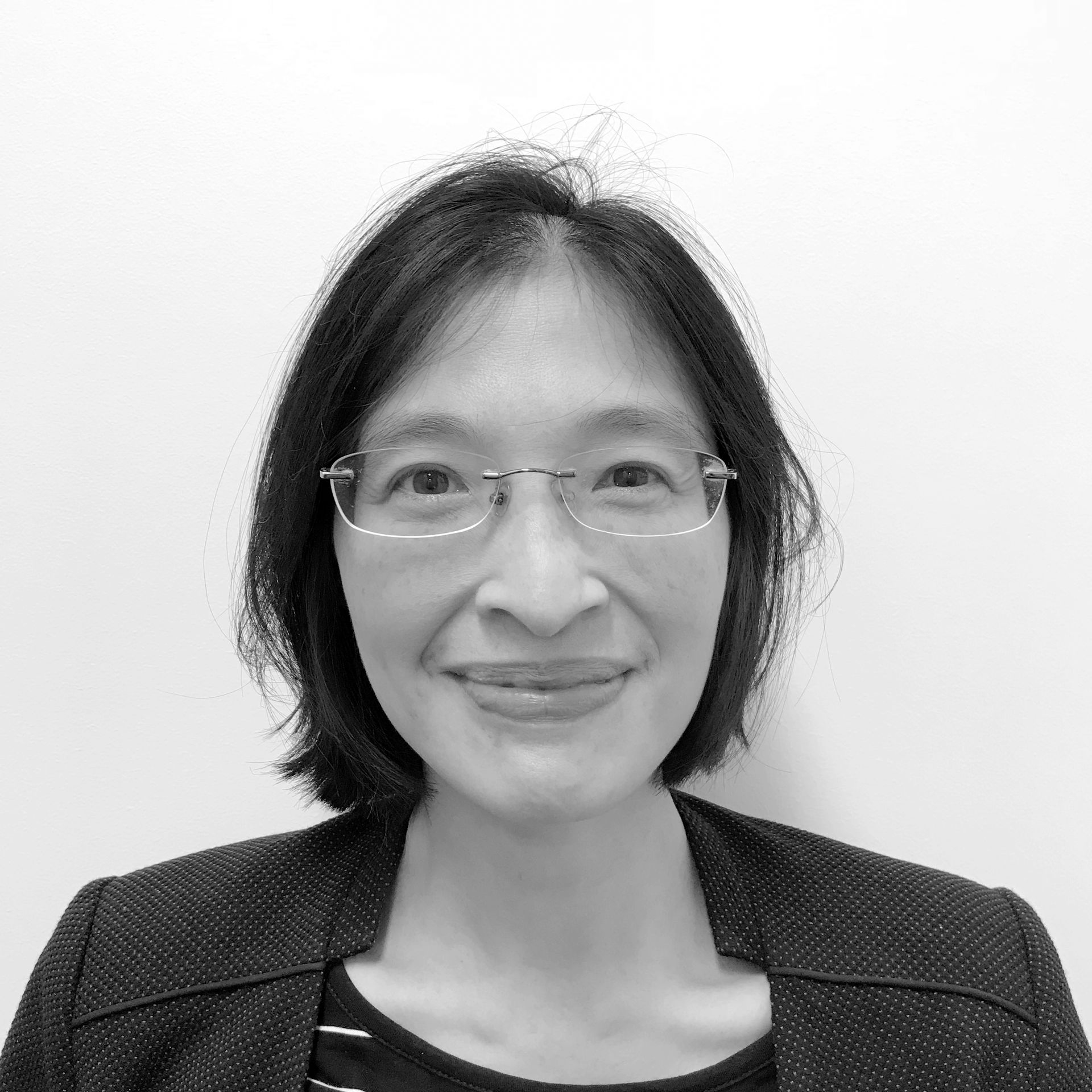 A woman wearing glasses and a jacket is smiling in a black and white photo.