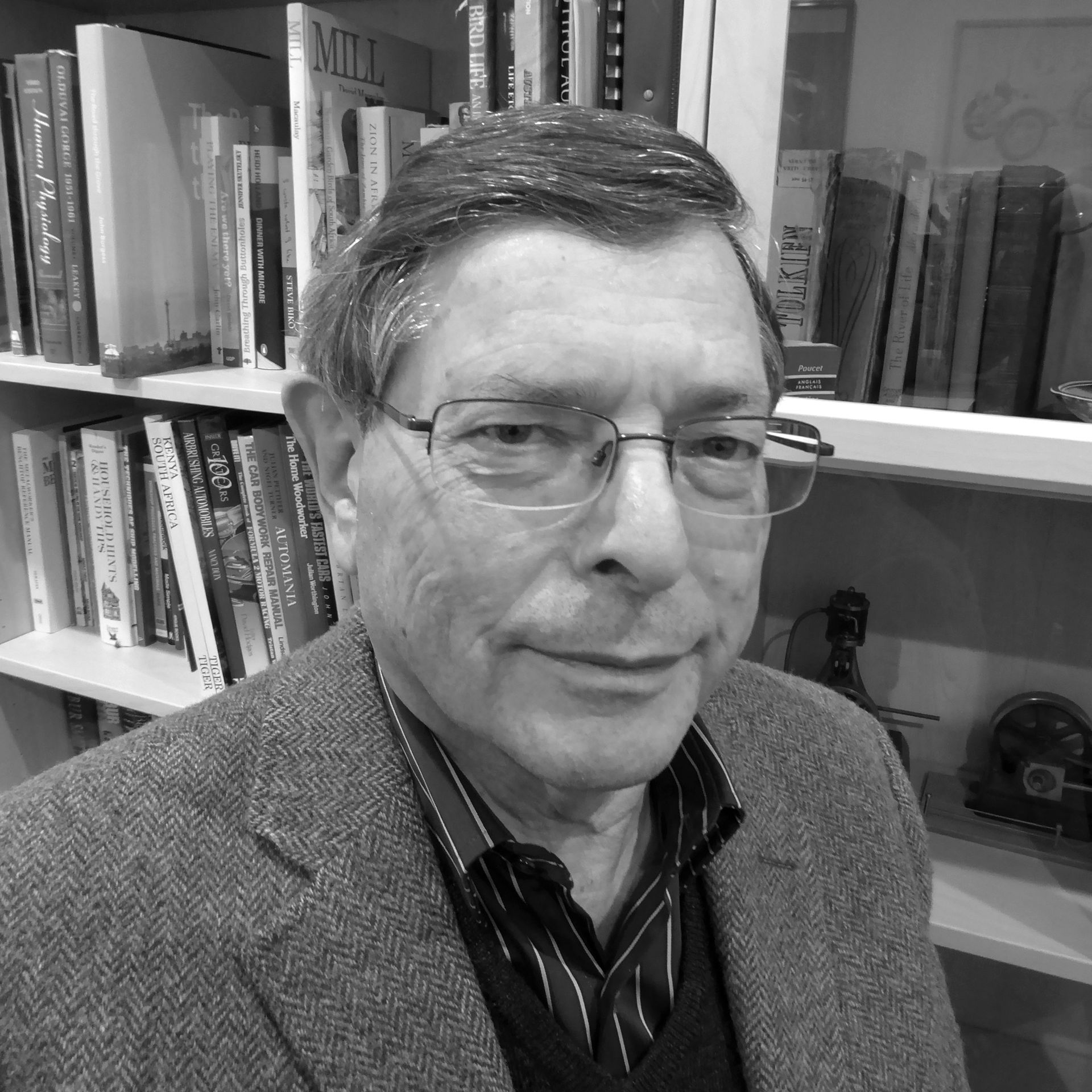 A man wearing glasses is standing in front of a bookshelf