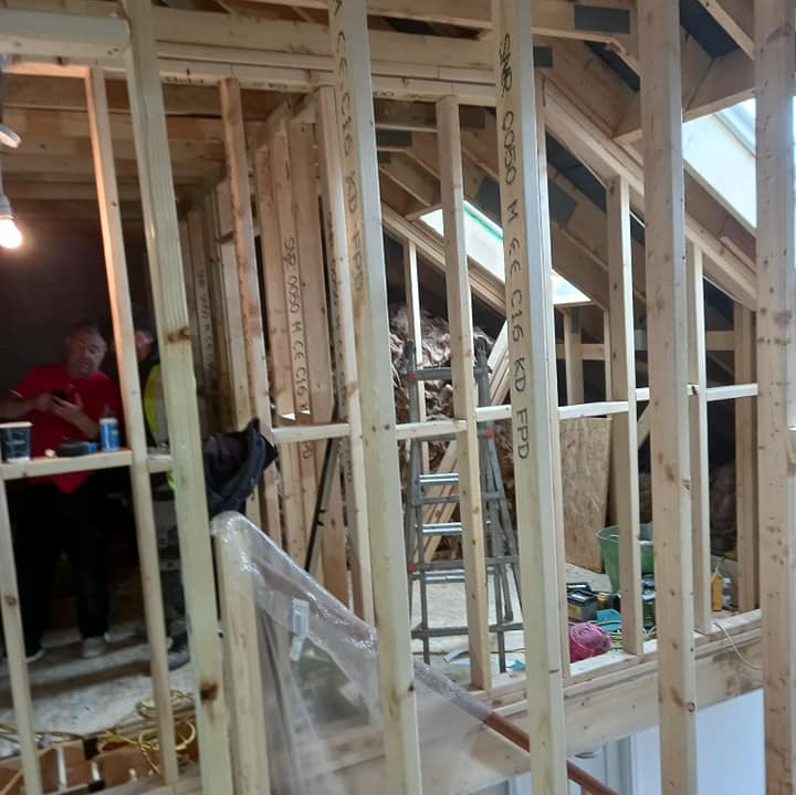 Interior view of wooden framing during construction in a room, with people working.