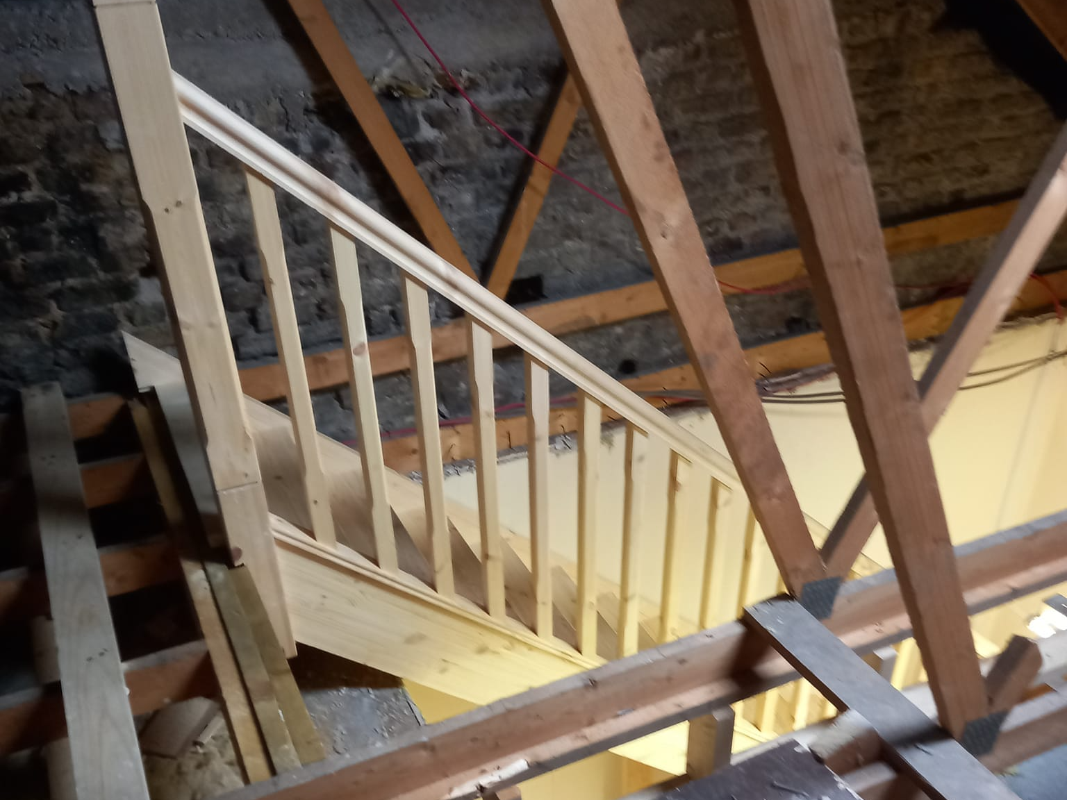Wooden staircase under construction in an attic, featuring a railing with spindles.