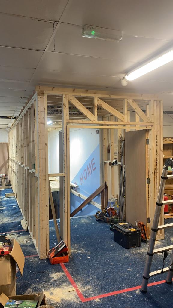 Interior construction: wooden frame walls and door. Tools and debris on blue carpet.
