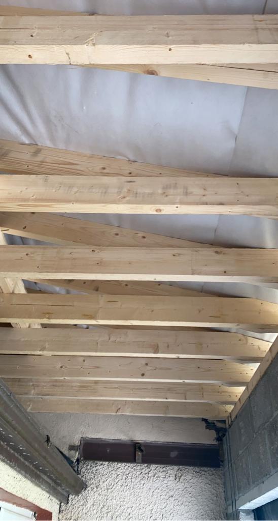 Wooden rafters installed on a structure, covered with a white tarp.