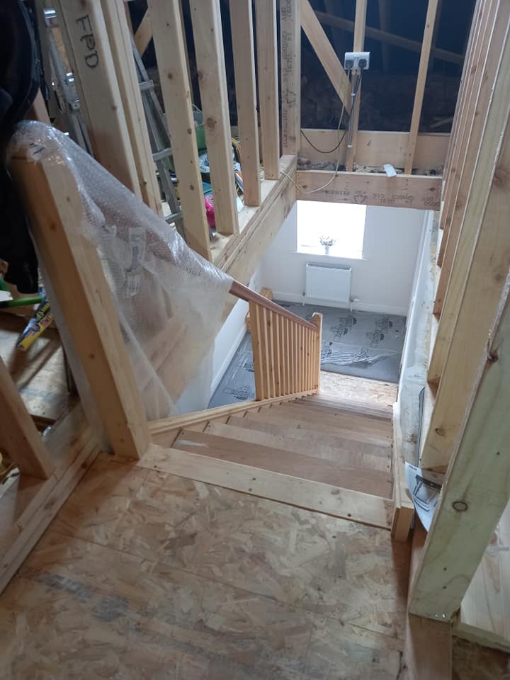 Wooden staircase under construction. Handrail installed. Framing visible. Window at the bottom.