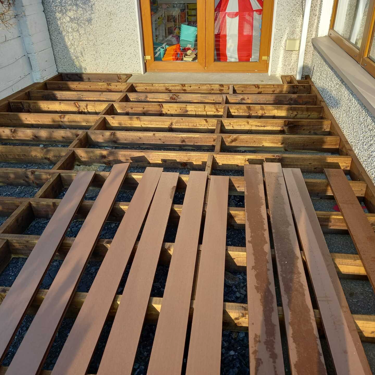 Wooden deck under construction; brown planks laid on a wooden frame in front of a doorway.