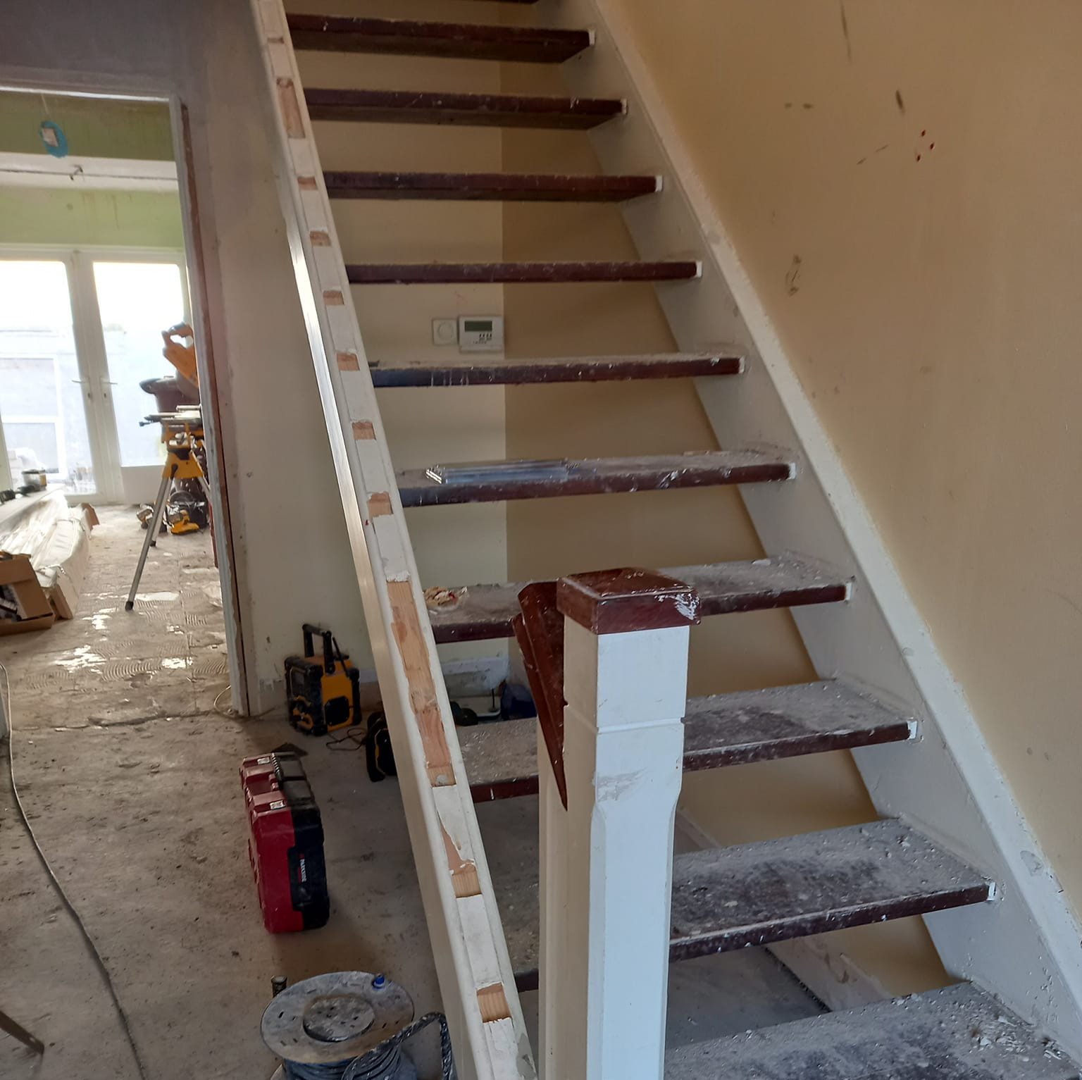 Wooden staircase with white banister, undergoing renovation.