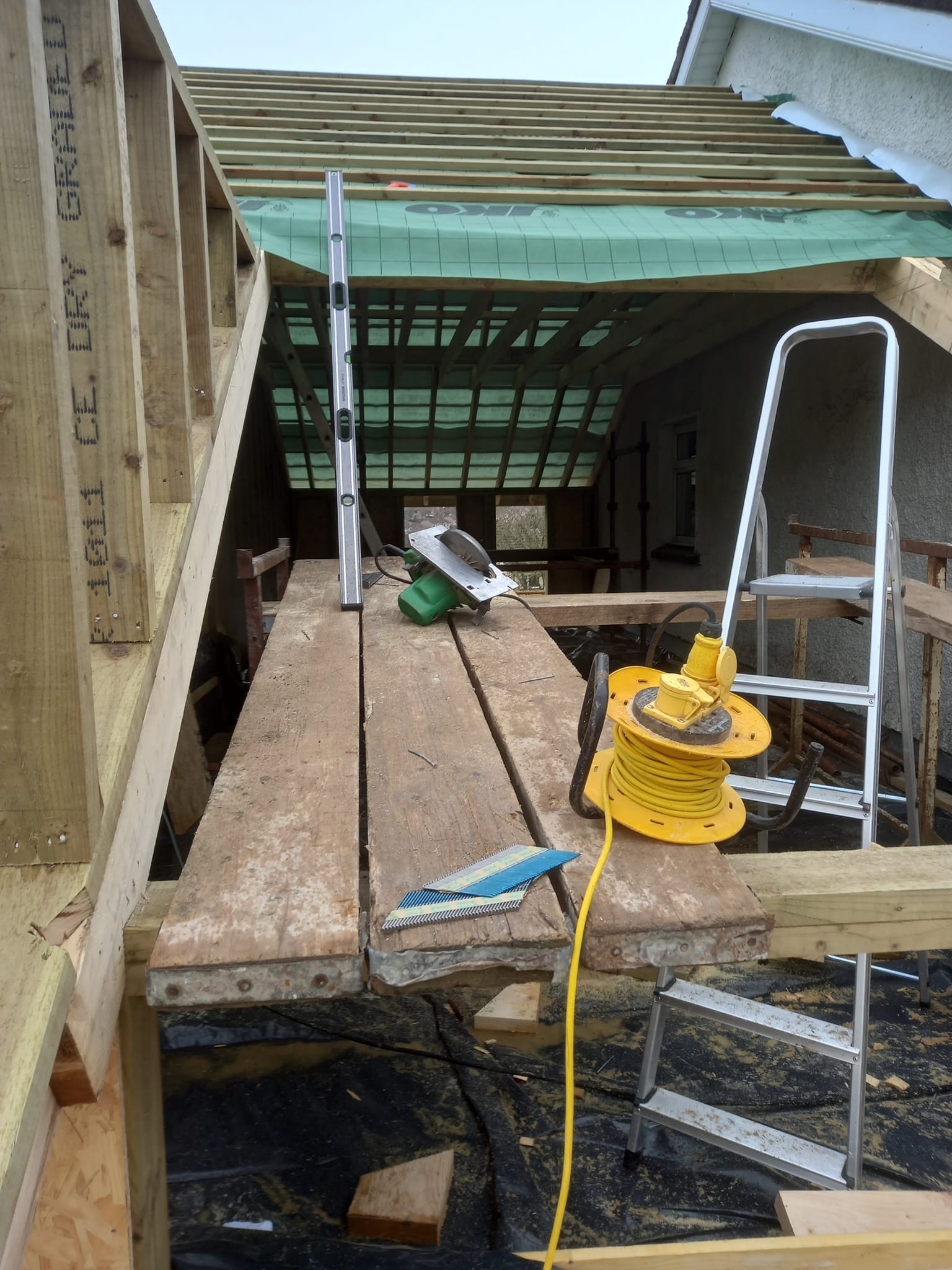 Construction site: unfinished roof, wooden beams, tools, and a yellow extension cord.