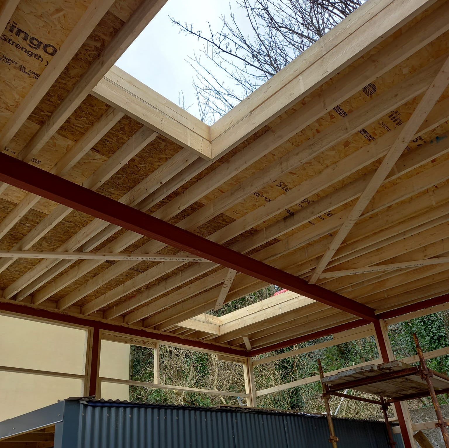 Wooden roof frame with skylights, red metal beams, under construction.
