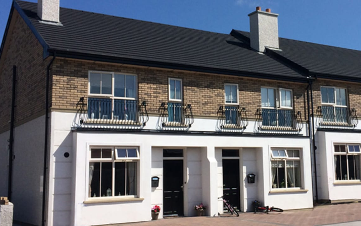 Row of brick and white townhouses with dark roof and black doors.