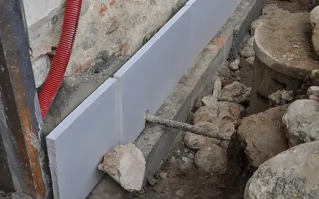 A piece of styrofoam is sitting on the ground next to a stone wall.