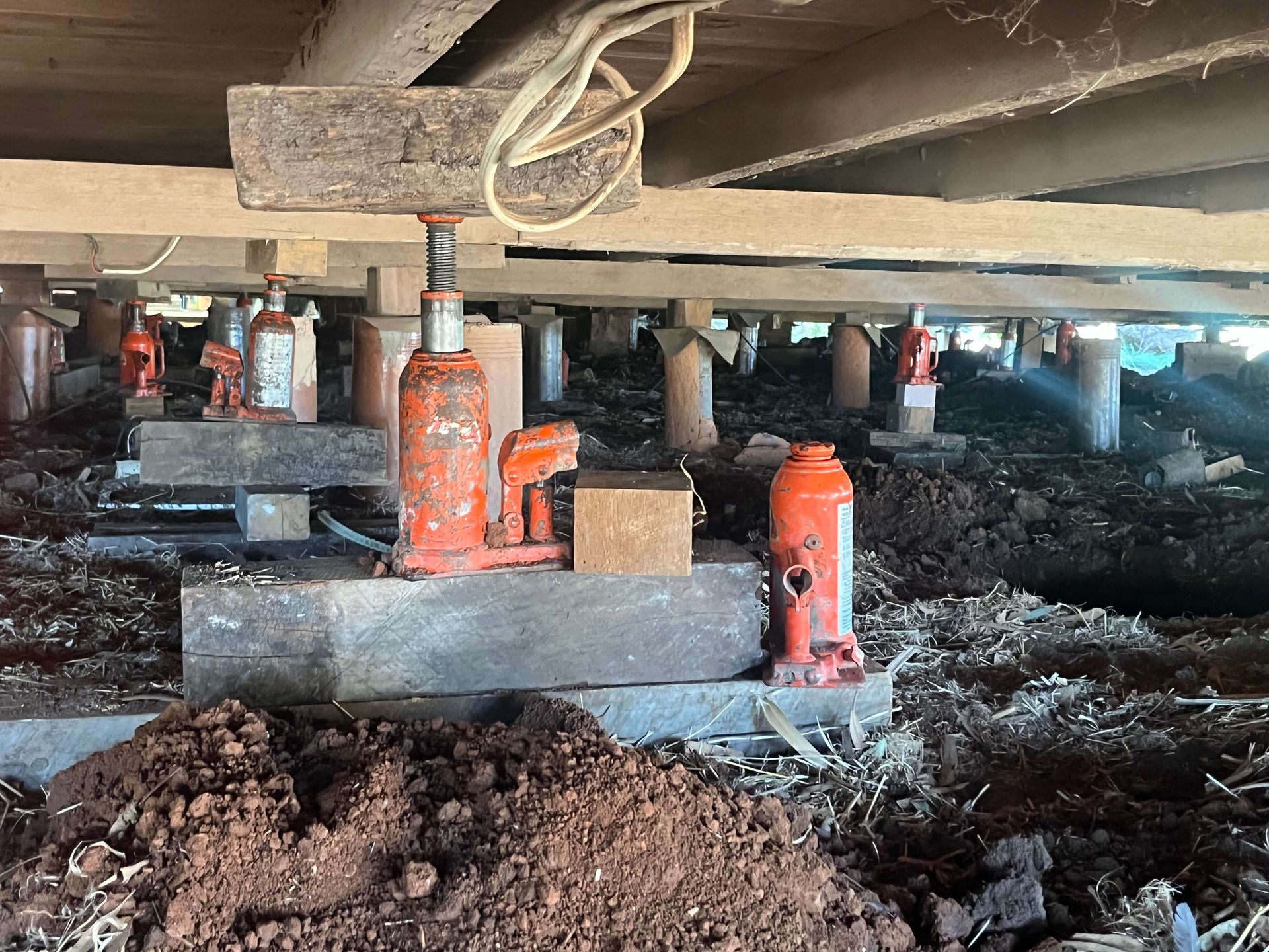 A hydraulic jack is sitting on top of a pile of dirt under a bridge.