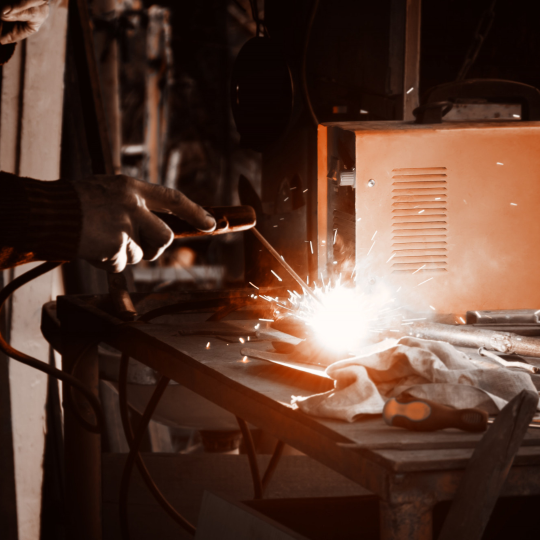Welder at work, sparks flying, using a welding torch on metal in a workshop.