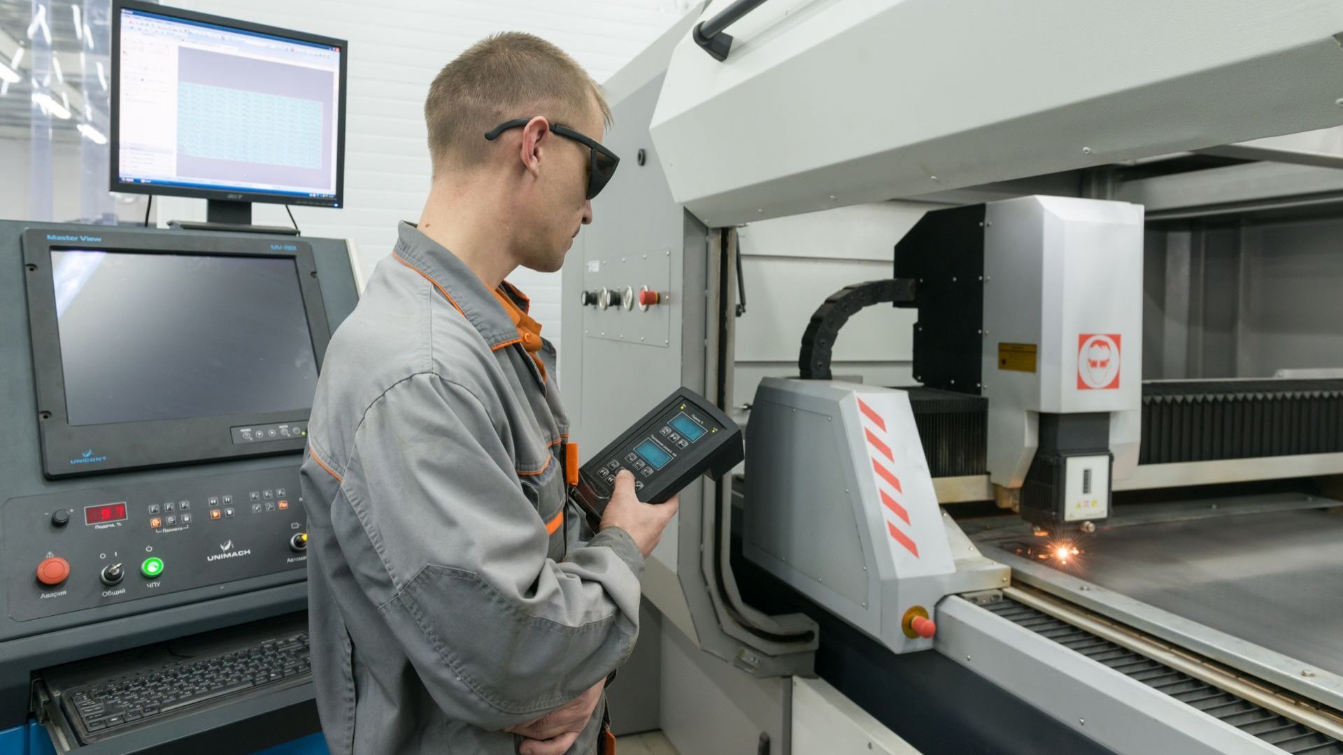 Man operating a CNC machine, wearing safety glasses. He is in a factory setting.