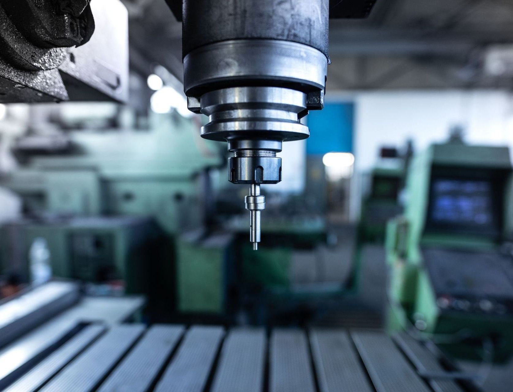 Close-up of a CNC machine head with a tool in a factory setting, other machines blurred in the background.