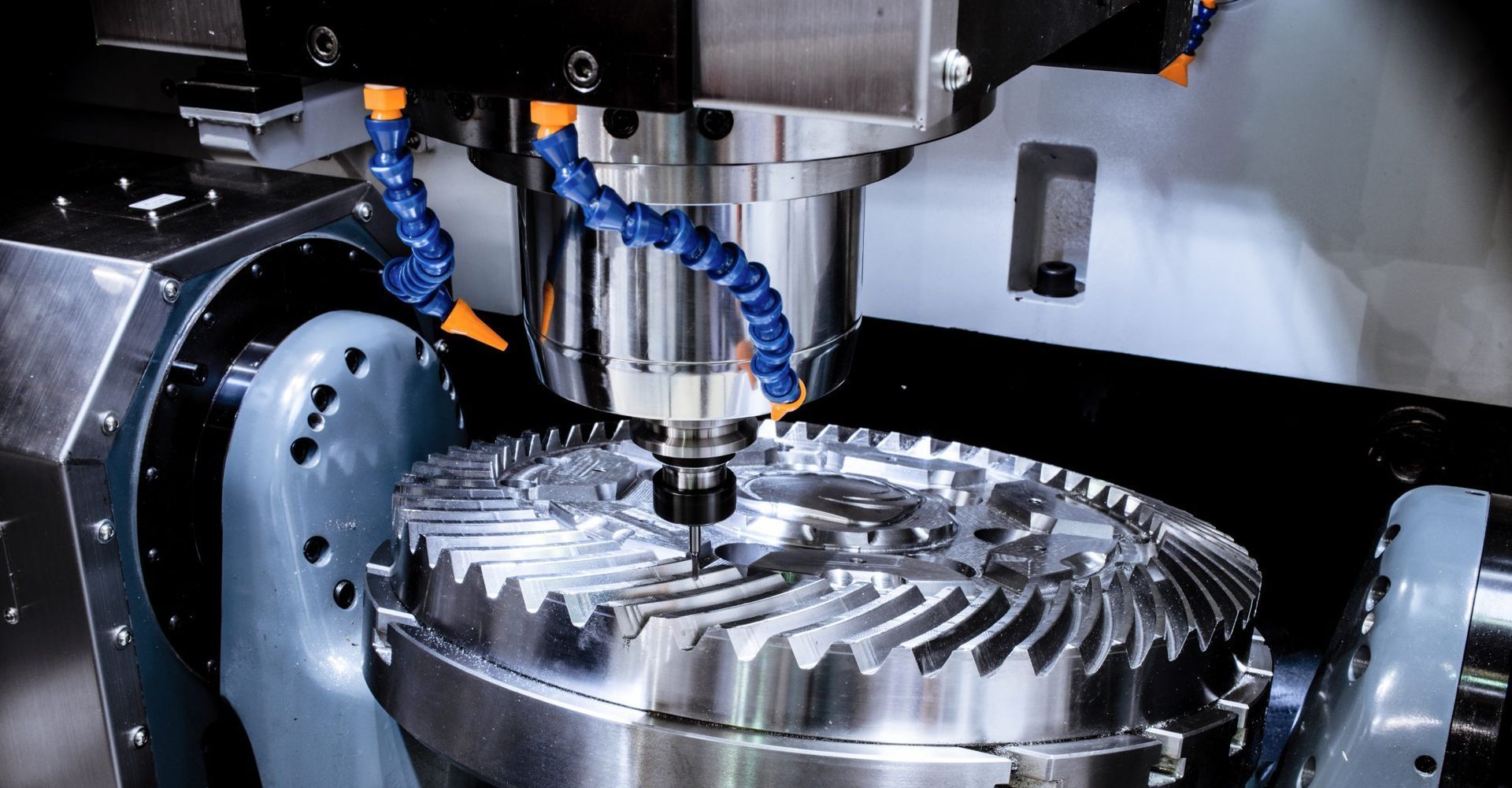 CNC machine cutting teeth into a large metal gear. Coolant lines visible.