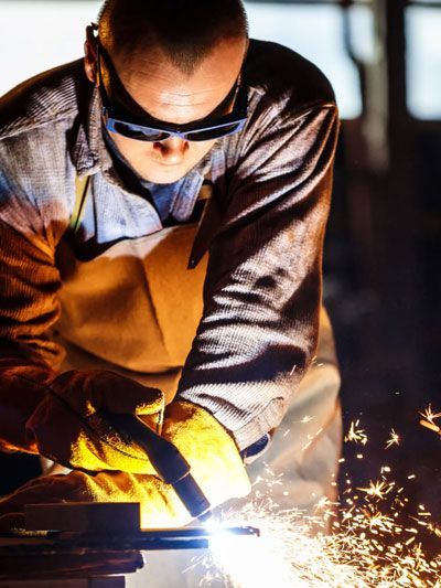 Welder wearing safety glasses and gloves, working with sparks in workshop.