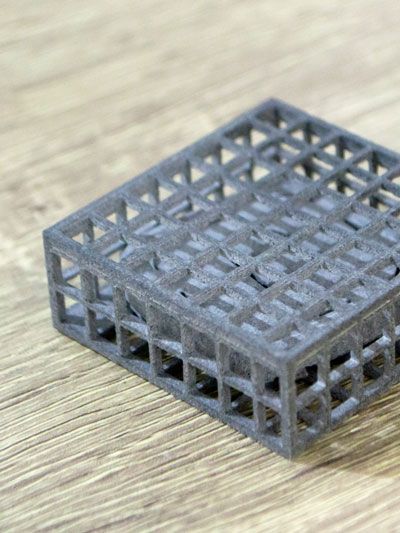Gray, lattice-structured cube on a wooden surface.