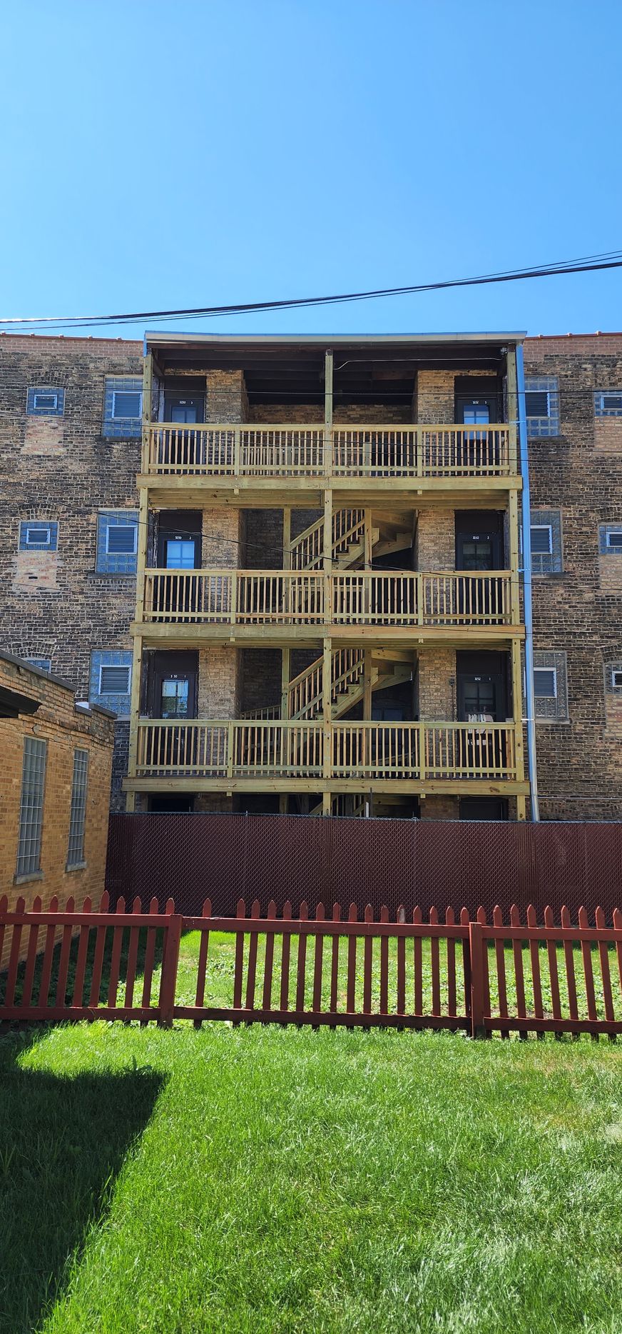 A large building with a lot of windows and balconies is behind a fence.