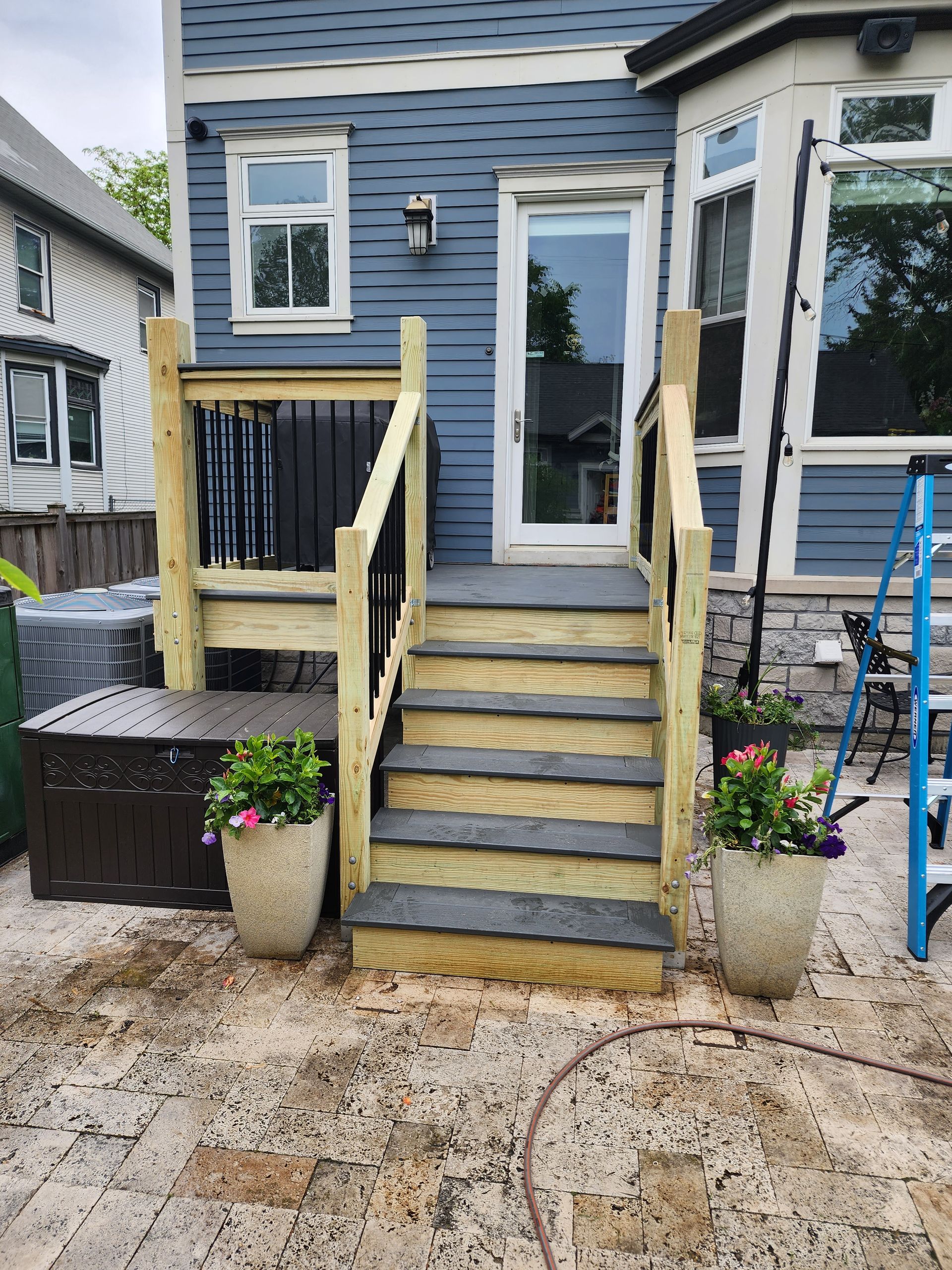 A wooden deck with stairs is being built in front of a blue house.