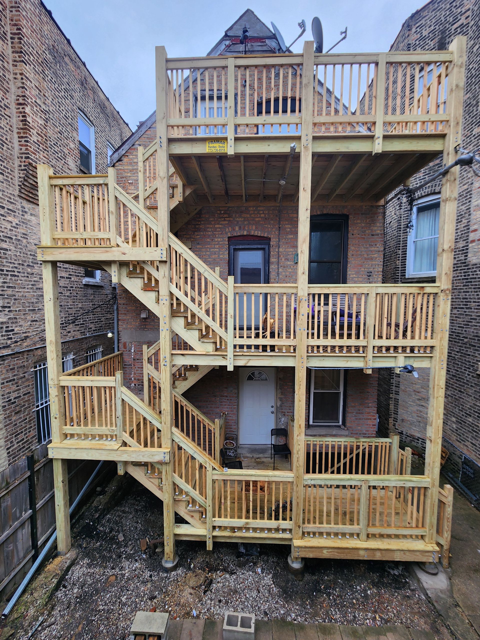 A wooden deck with stairs leading up to it is in front of a brick building.