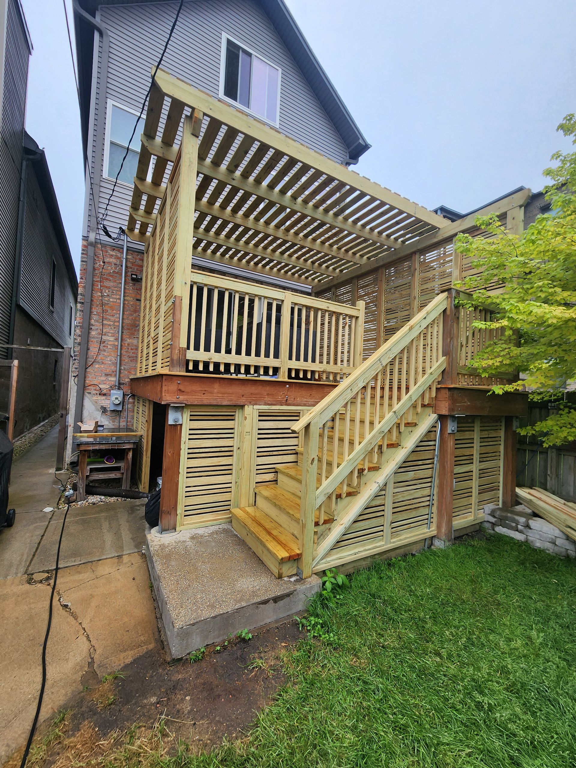 A wooden deck with stairs leading up to it is in the backyard of a house.