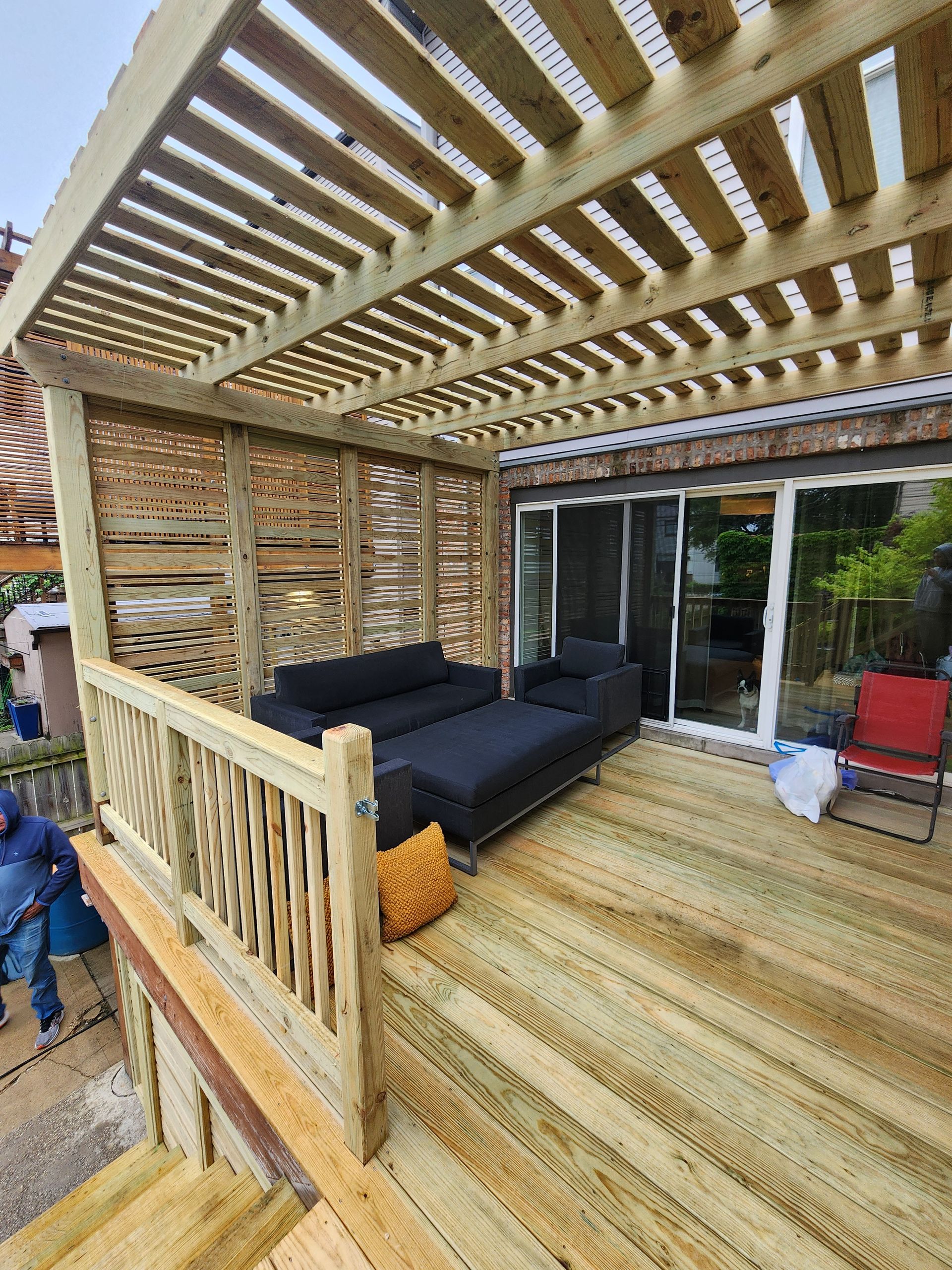 A wooden deck with a couch and chairs under a pergola.