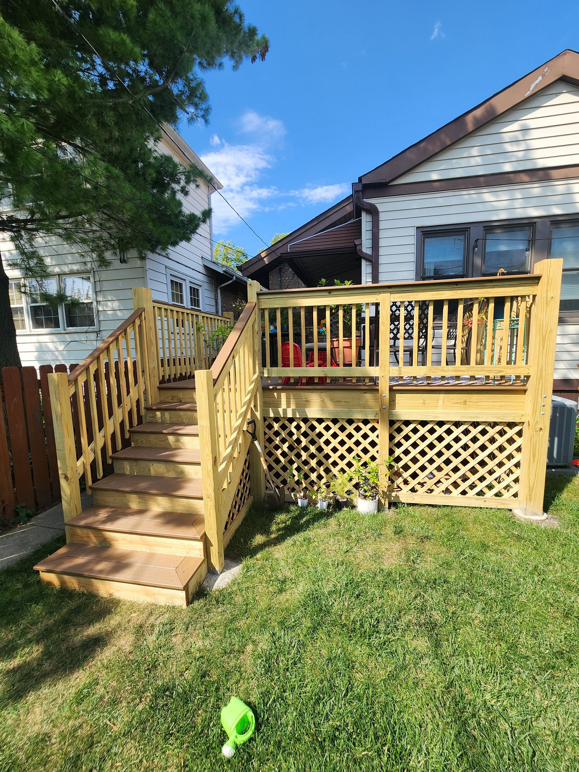 A wooden deck with stairs leading up to it is in the backyard of a house.