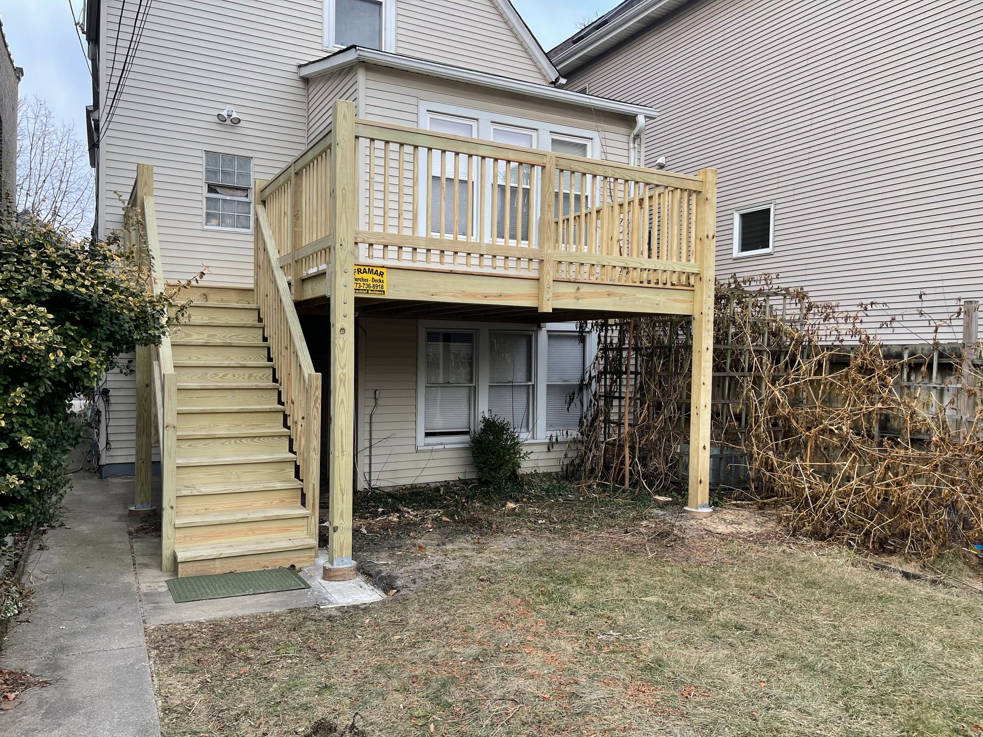 A wooden deck with stairs leading up to it is in the backyard of a house.