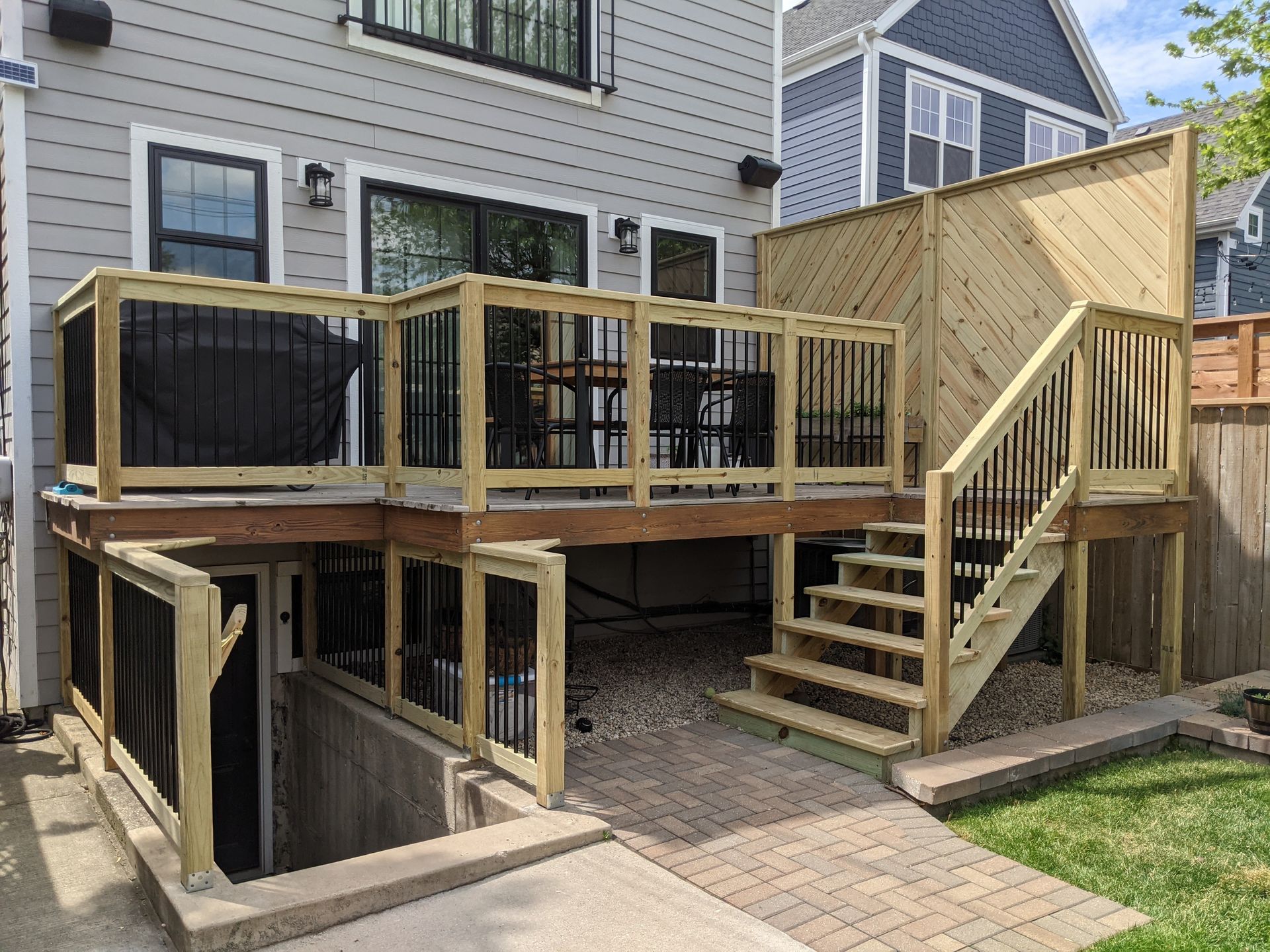 A wooden deck with stairs leading up to it is in the backyard of a house.