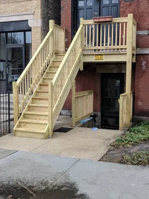 A wooden staircase leading up to a balcony on the side of a building.