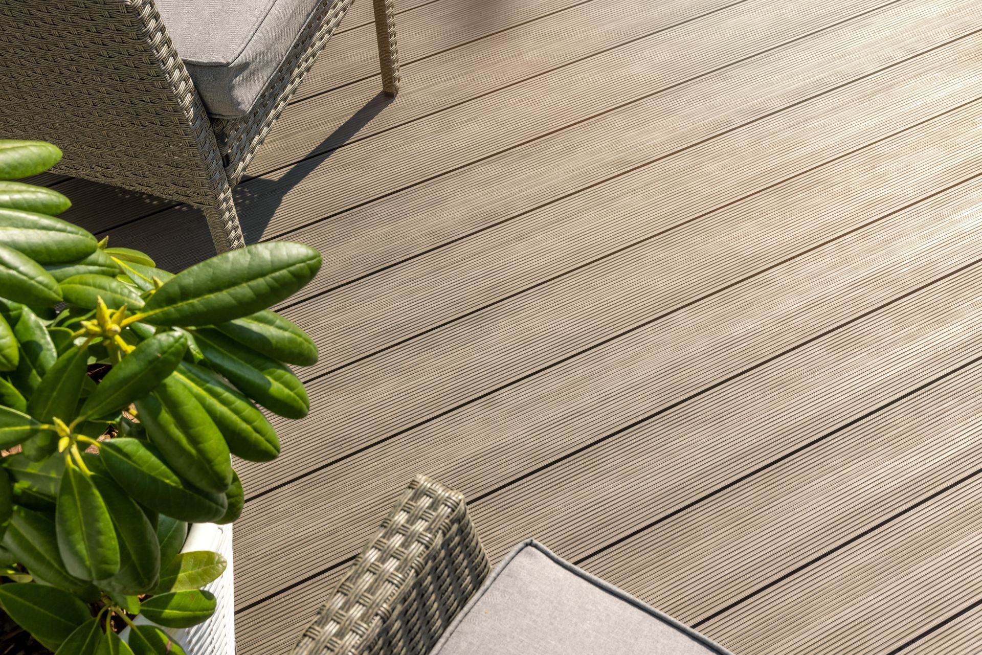 Modern composite decking surface surrounded by outdoor furniture and decorative greenery.