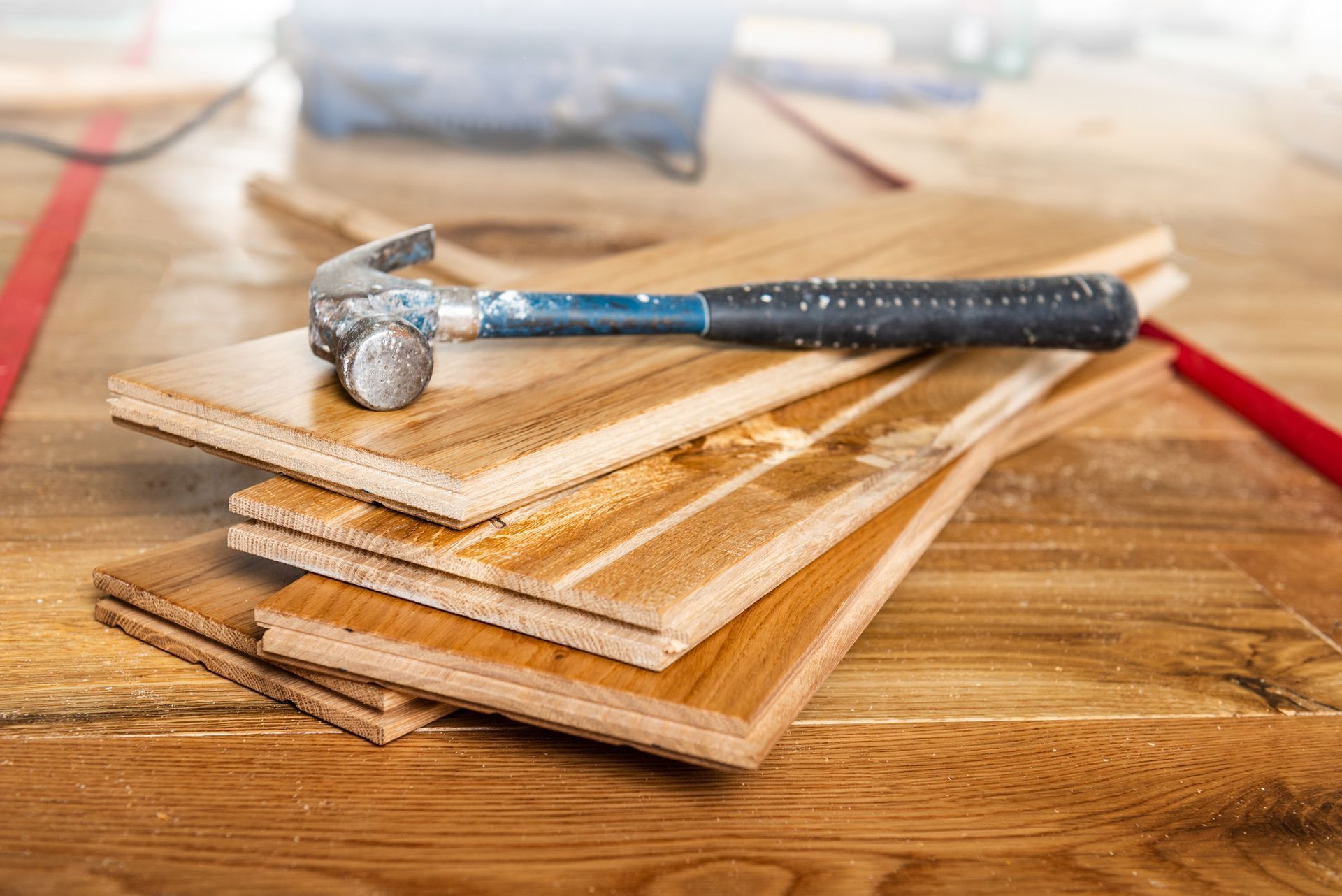 Hammer resting on stacked wooden planks for flooring installation in carpentry workshop.