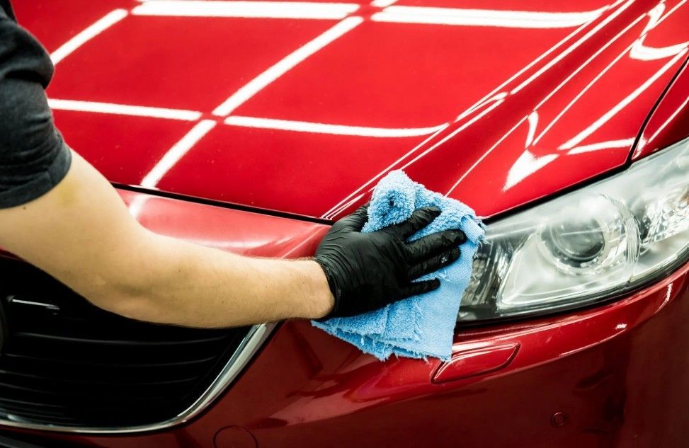 Person wiping a red car’s headlight with a blue cloth during cleaning