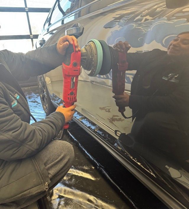 Technician using a suction cup tool to repair a dark car door in a garage