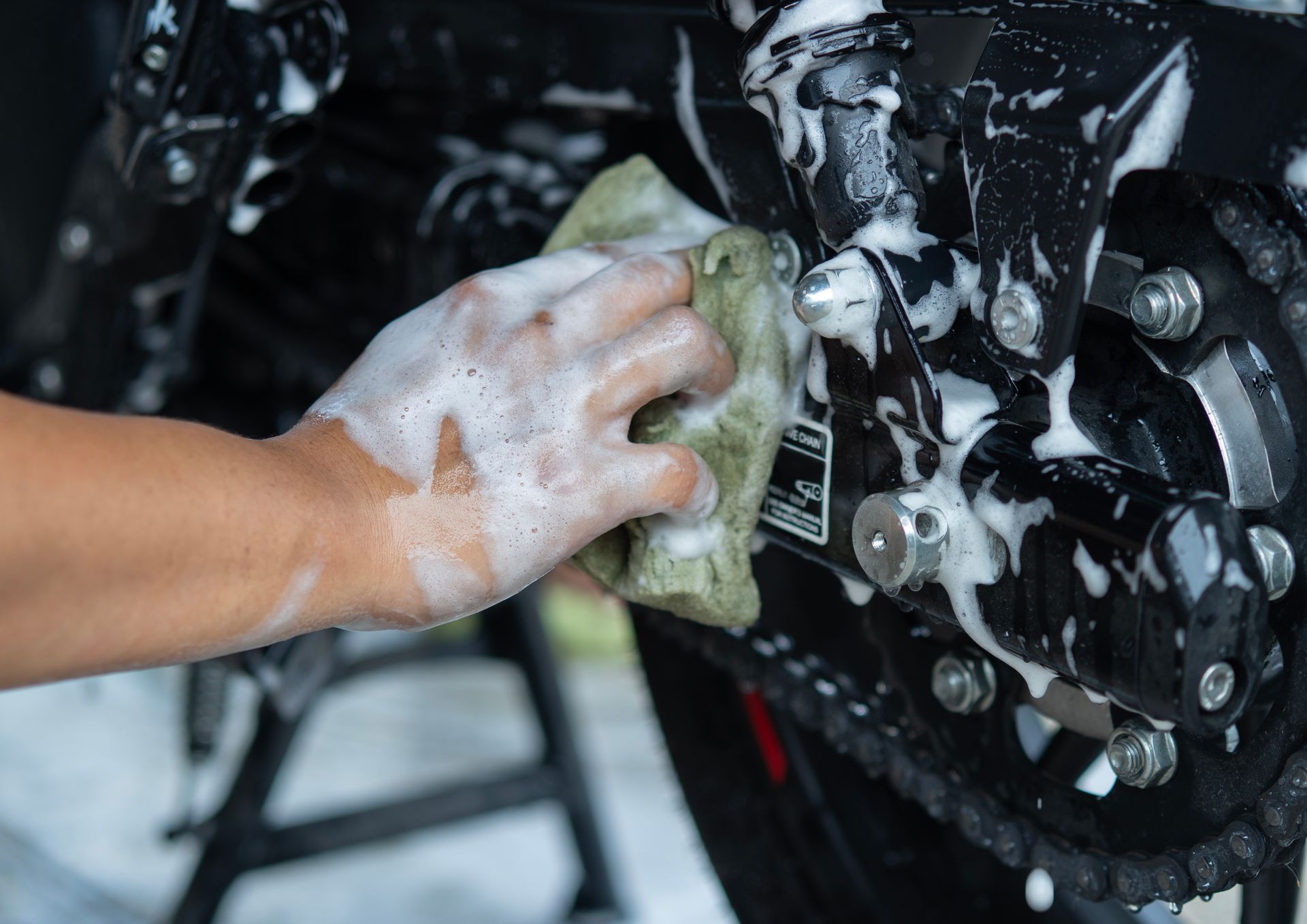 Hand washing a black motorcycle engine with soapy foam and a green cloth