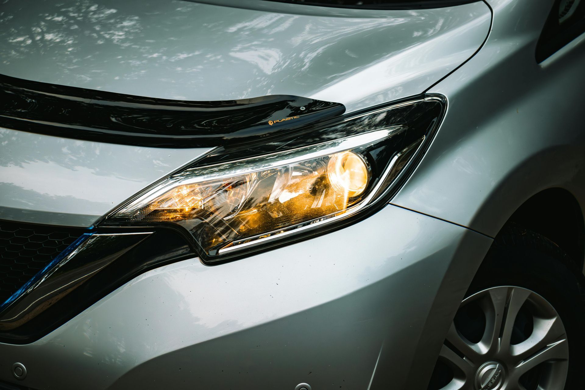 Silver car headlight illuminated, part of the front body and wheel visible.
