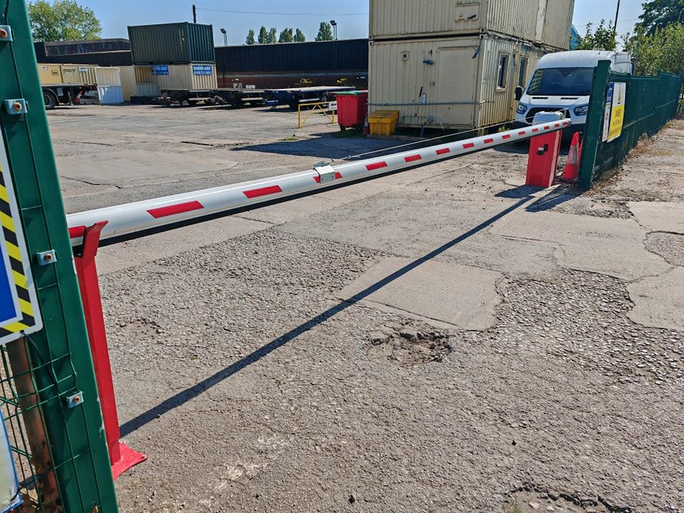 A red and white striped barrier arm blocks an asphalt entrance. A white van is parked inside.