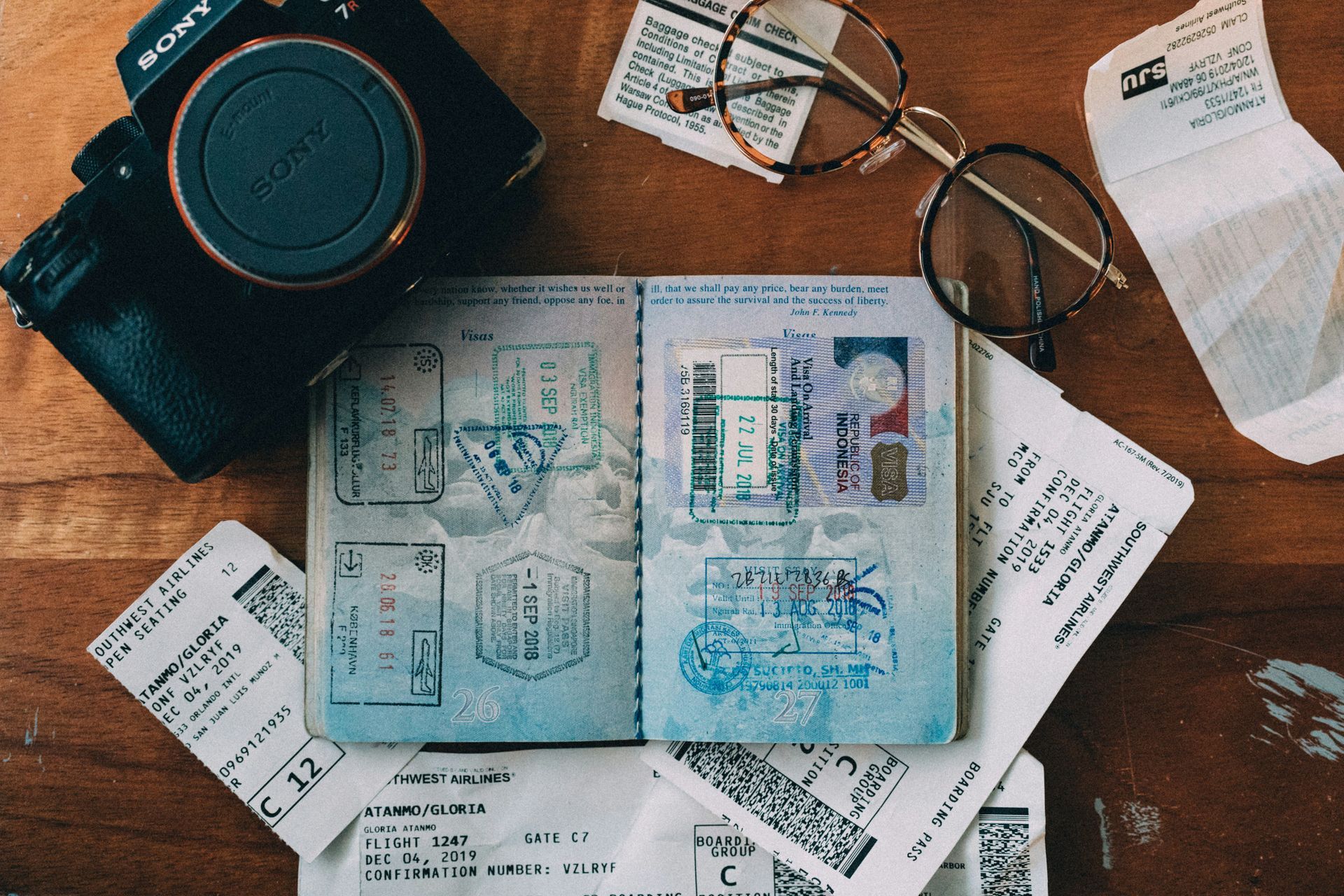 A Sony camera, passport with stamps, eyeglasses, and boarding passes on a wooden surface.