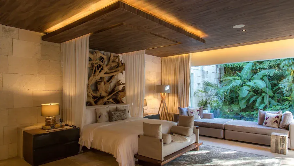Modern hotel bedroom with a canopy bed, warm wood accents, and a large tropical-view window